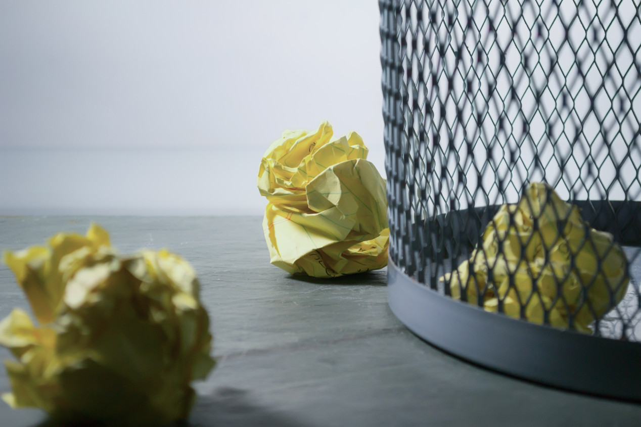 A photo of an mesh office trash can, with some crumpled up papers inside.